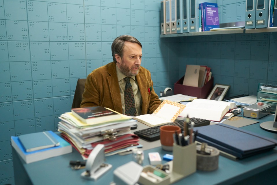 David Mitchell sitting at a desk in an office, reviewing papers.