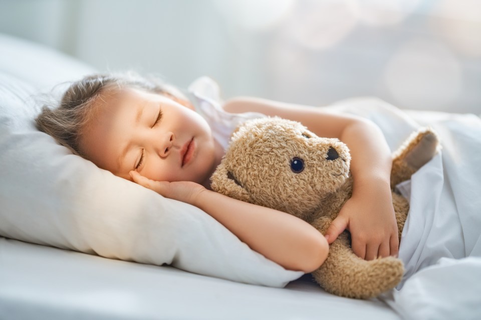Child sleeping in bed with teddy bear.