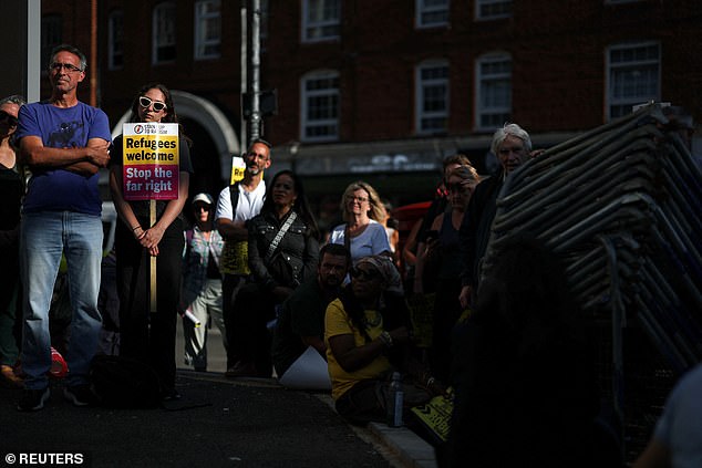 Stand Up To Racism activists stand outside hotel holding a 'Refugees welcome' sign during a counter demonstration on August 8, 2025