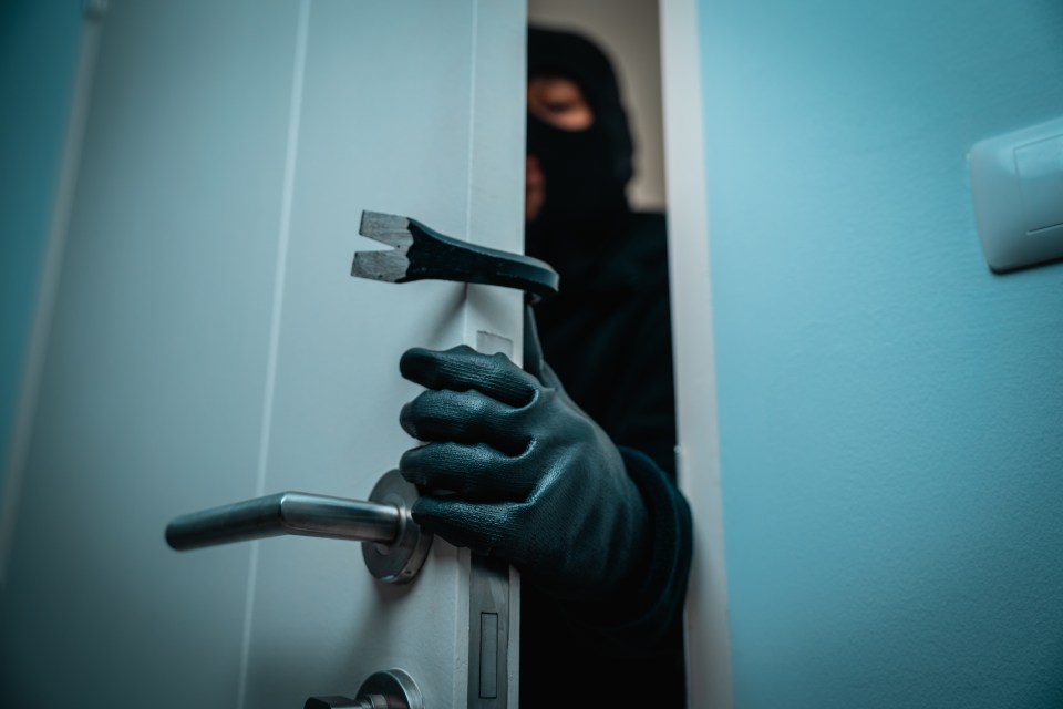 A burglar using a crowbar to break into a house.