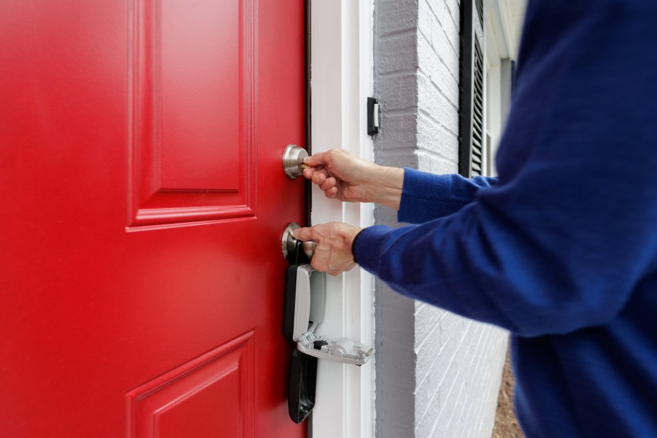 Person unlocking a red door with a key from a lockbox.
