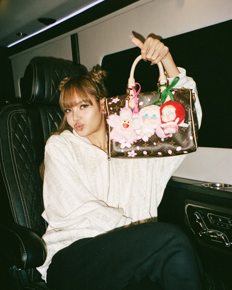 Lisa from Blackpink in a car, showing off her Louis Vuitton handbag with charms.