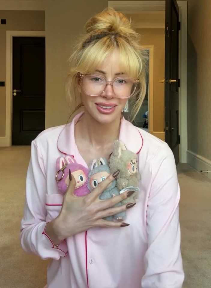 Woman in pajamas holding three Labubu dolls.