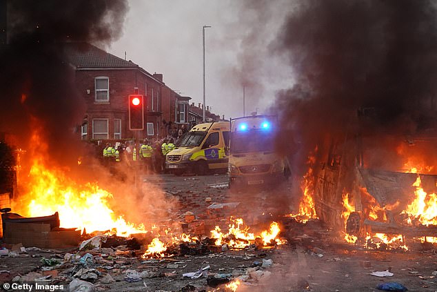 Riot police hold back protesters near a burning police vehicle after disorder breaks out in Southport on July 30, 2024