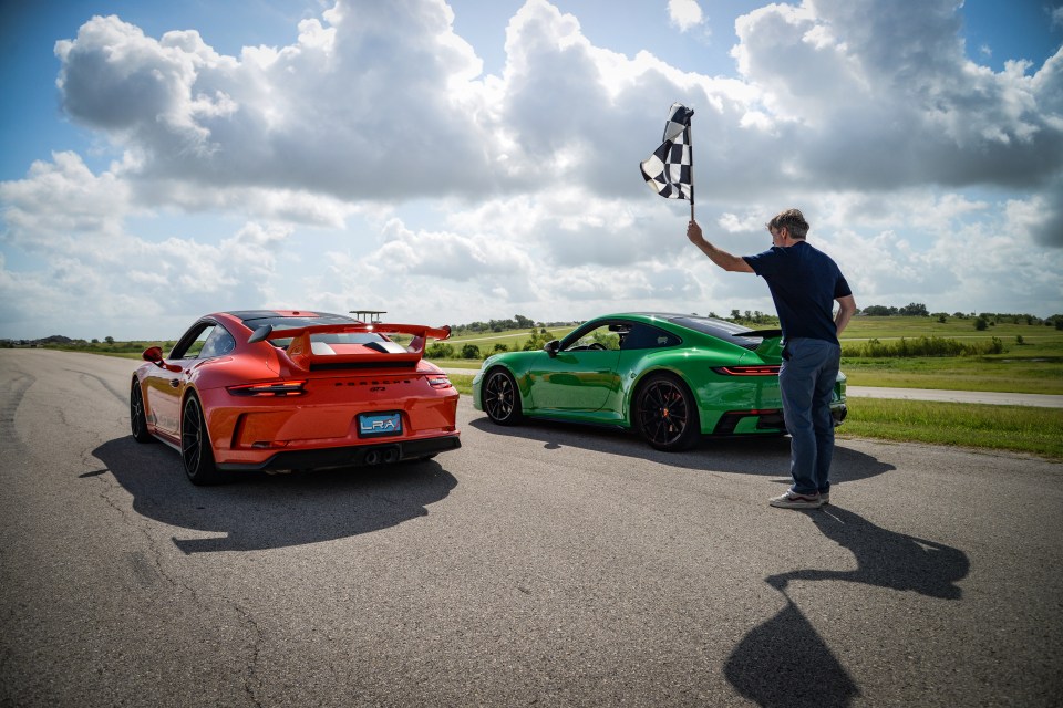 A man waves a checkered flag near two Porsches at a race track.