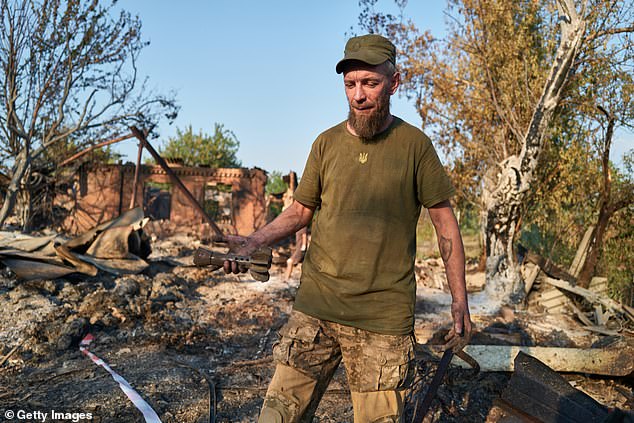 Ukrainian soldier holds the remains of a shell at the site of a Russian Shahed drone strike that destroyed vehicles and residential buildings the previous day on August 20, 2025 in Sloviansk, Ukraine