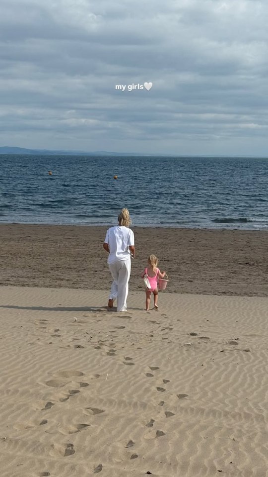 Woman and toddler walking on beach.