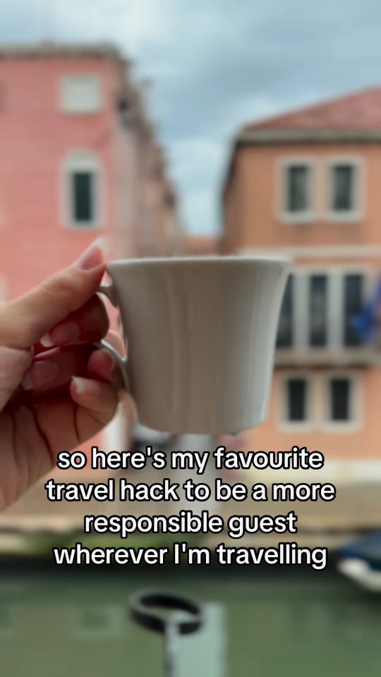 A hand holding a small white cup against a blurry background of Italian buildings.