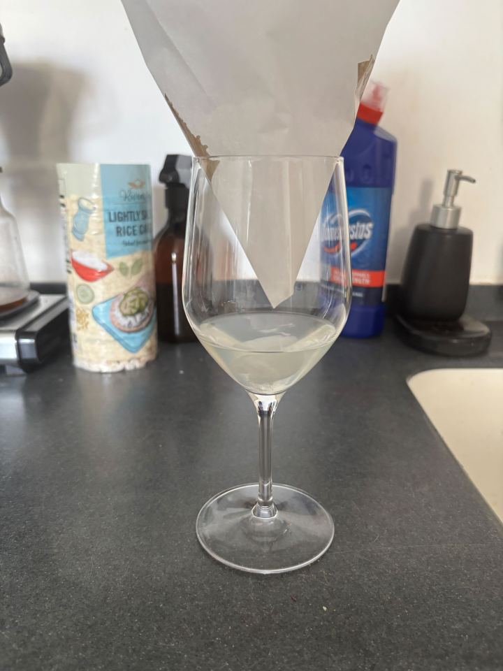 Wine glass with paper funnel and liquid inside.