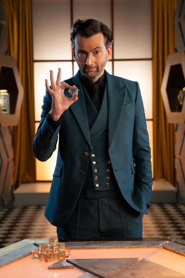 David Tennant holding a small cube on the set of a game show.