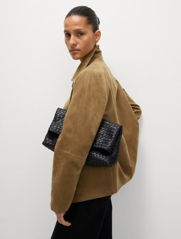 Woman wearing a brown suede jacket and carrying a black woven clutch.