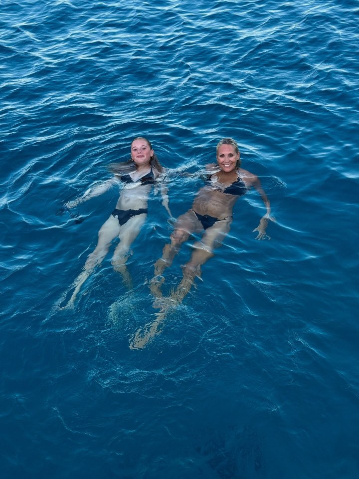 Jenni Falconer and her daughter in black bikinis floating in the ocean.
