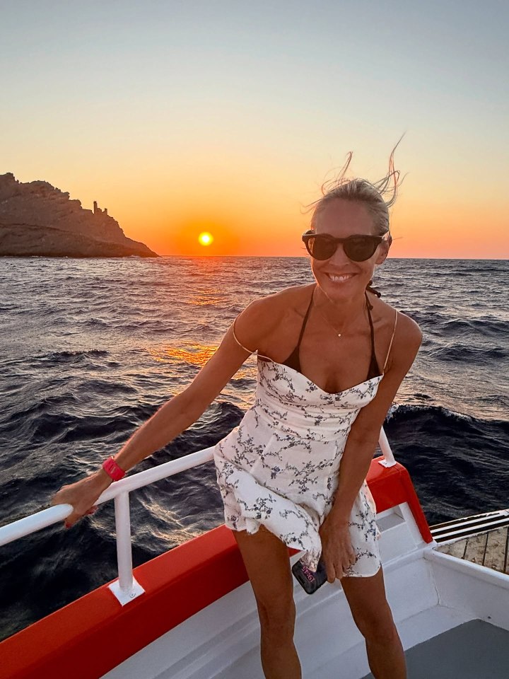 Woman in a white dress on a boat at sunset.