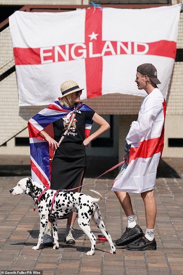 A man wearing an England flag while walking a Dalmatian