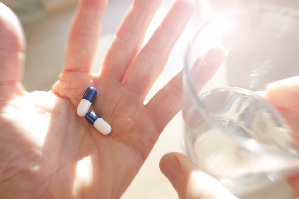 Hand holding two pills and a glass of water.
