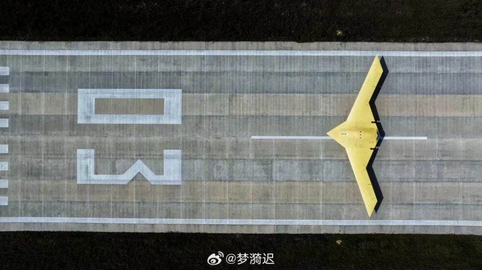 Aerial view of a large, yellow stealth flying wing aircraft on a runway.