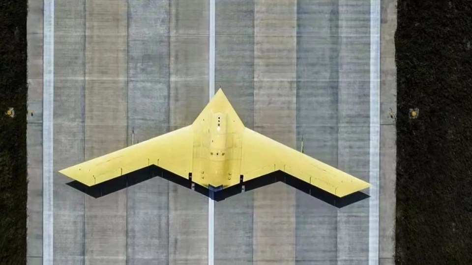 Aerial view of a large, yellow, stealth flying wing aircraft on a runway.