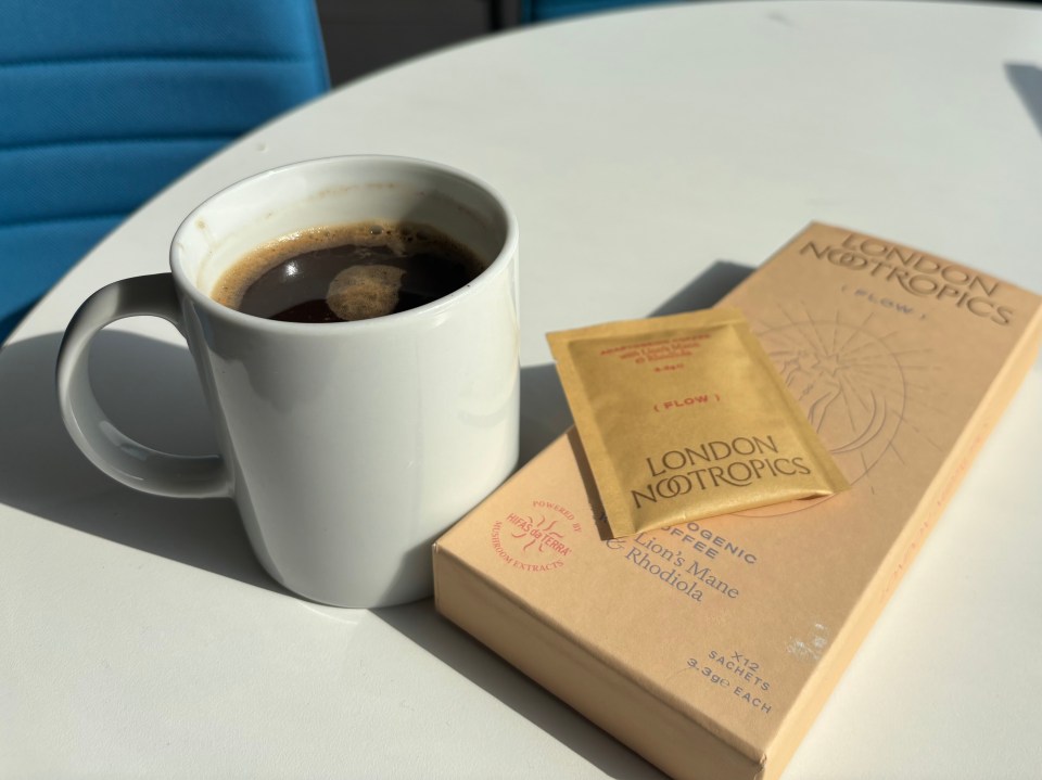 A mug of coffee next to a box of London Nootropics Flow coffee sachets.