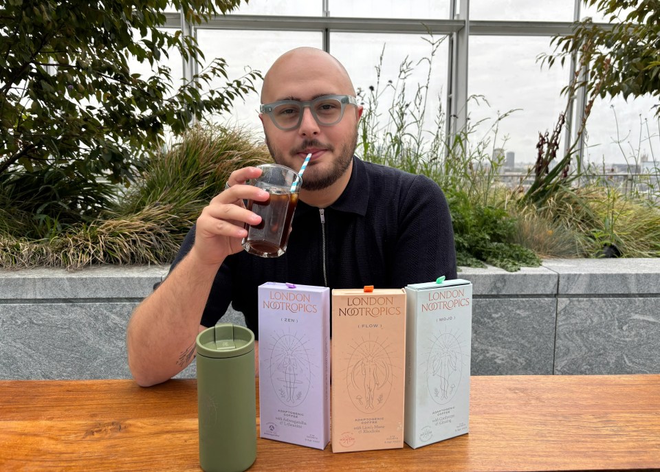 Person drinking iced coffee with London Nootropics boxes on a table.
