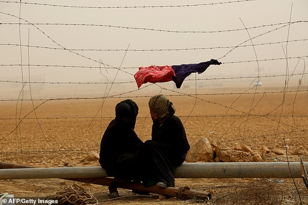 Syrian women sit next to the fence during a sandstorm at a temporary refugee camp in the village of Ain Issa, housing people who fled Islamic State group's Syrian stronghold Raqa