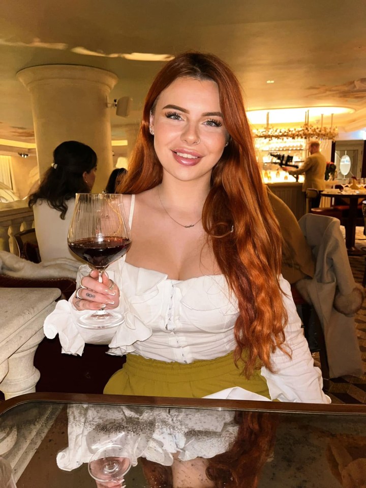 Woman with long red hair holding a glass of red wine in a restaurant.