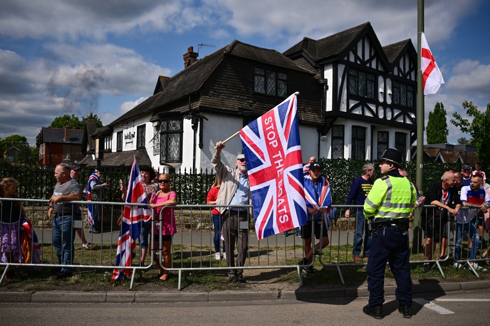 Protestor holding a Union Jack flag reading "Stop the Boats" at an anti-immigration protest.