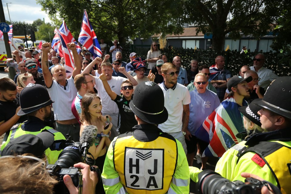 Police officers face a crowd of protestors waving Union Jack flags.