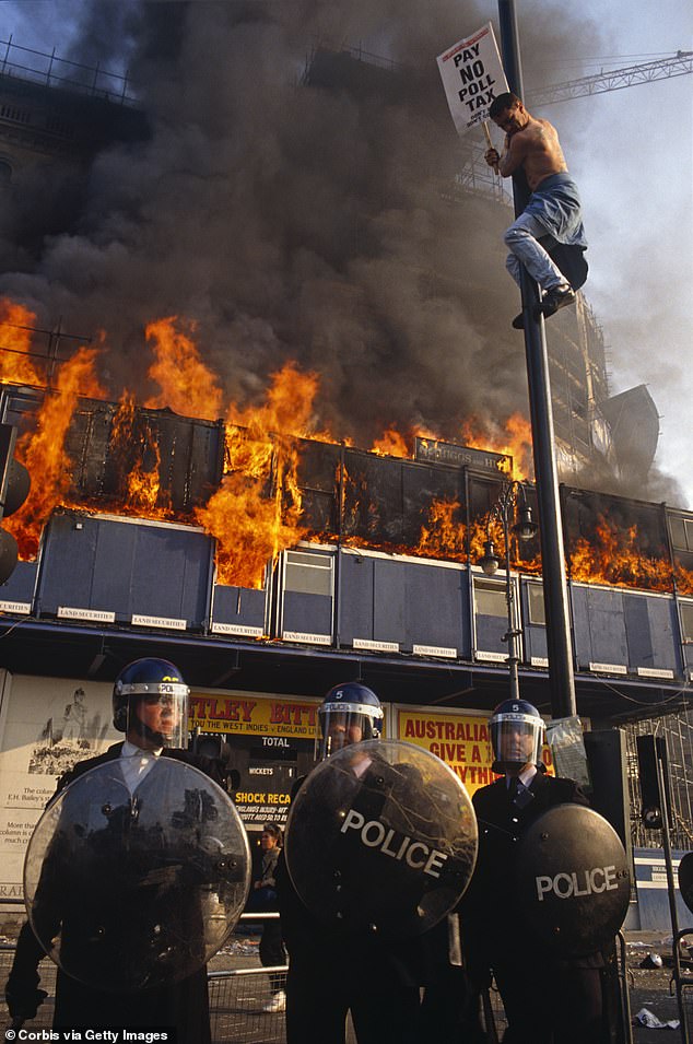 Pictured: A protestor hanging on a pole at the height of the Poll Tax Riot in 1990