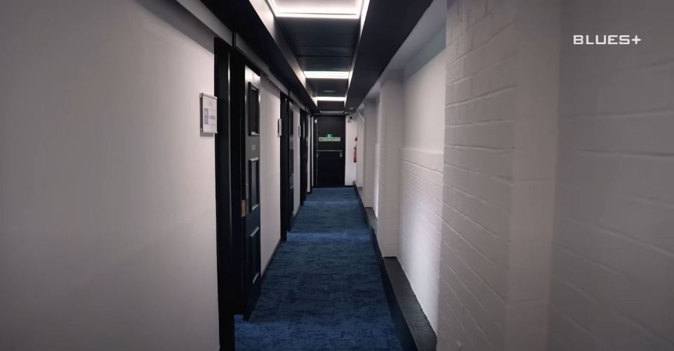 Long hallway with blue carpet and black doors.