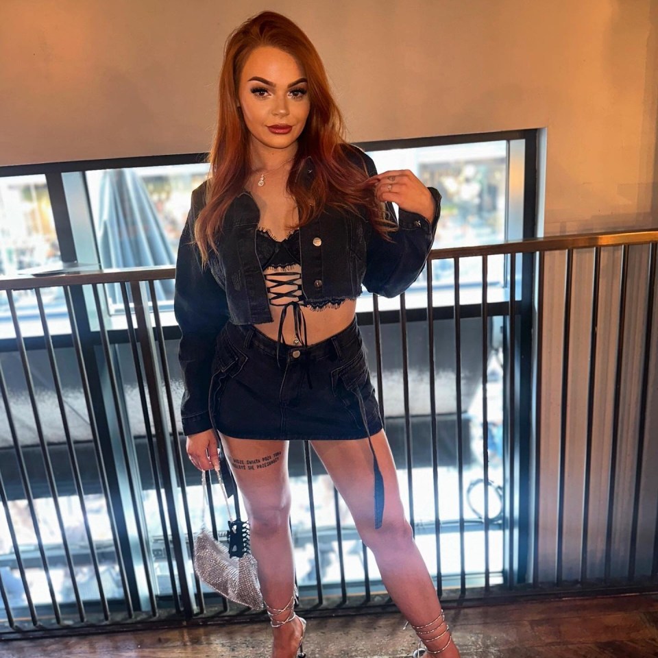 Woman with red hair wearing a denim jacket and skirt.