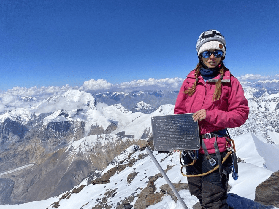 Woman on snowy mountain peak holding plaque.