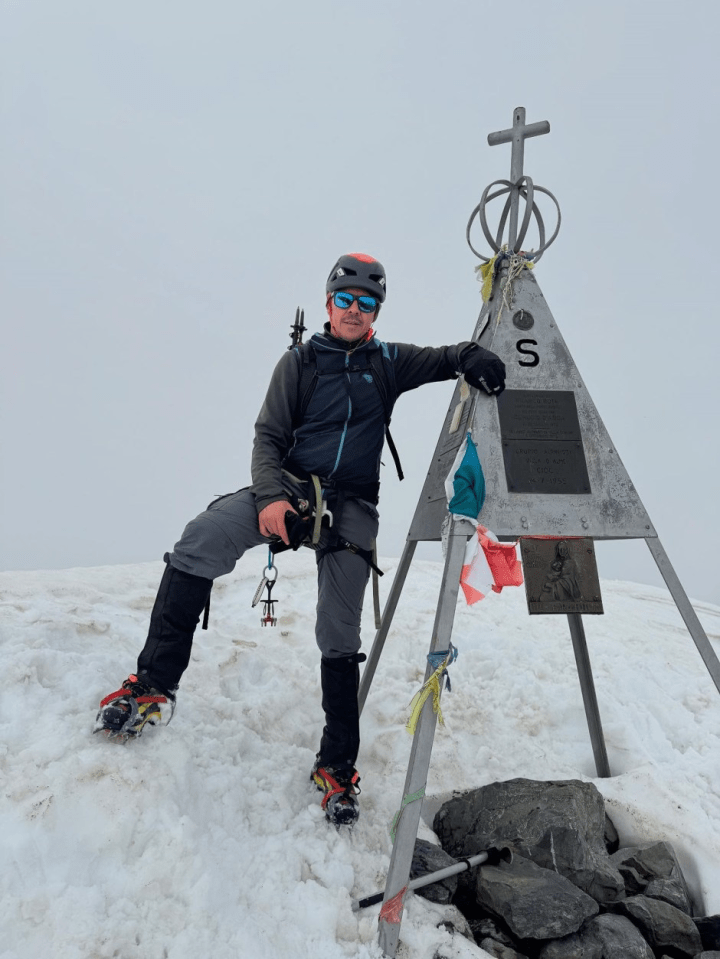 A mountain climber resting at a summit marker.