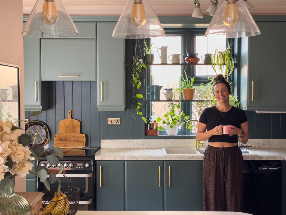 Woman standing in her teal kitchen holding a mug.