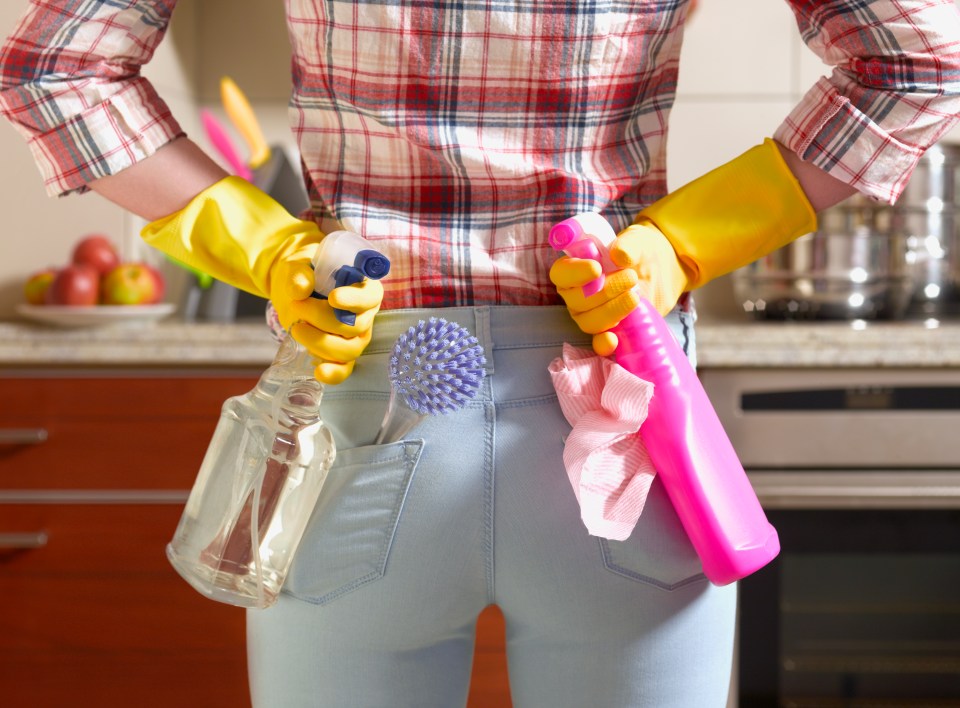 Woman wearing yellow cleaning gloves holding cleaning supplies.