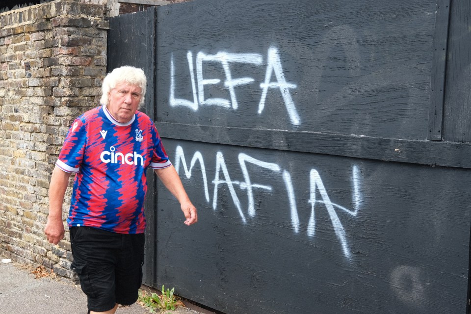 Graffiti reading "UEFA Mafia" on a wall, with a man in a Crystal Palace jersey walking by.