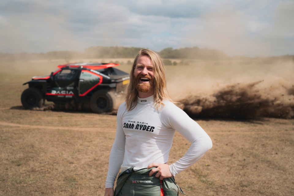 Sam Ryder smiling with a race car in the background.