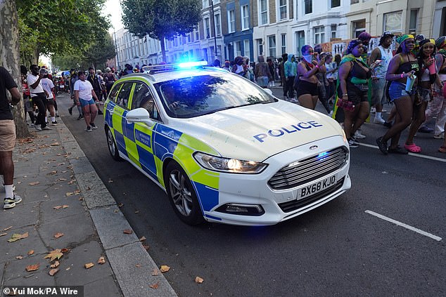 A police car drives past people taking part in J'ouvert ahead of the Children's Day Parade