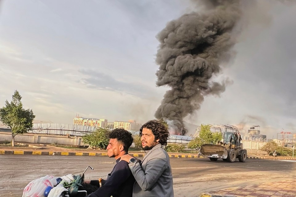 Two men on a motorbike watch a large plume of black smoke billowing from a fire in Sanaa, Yemen.