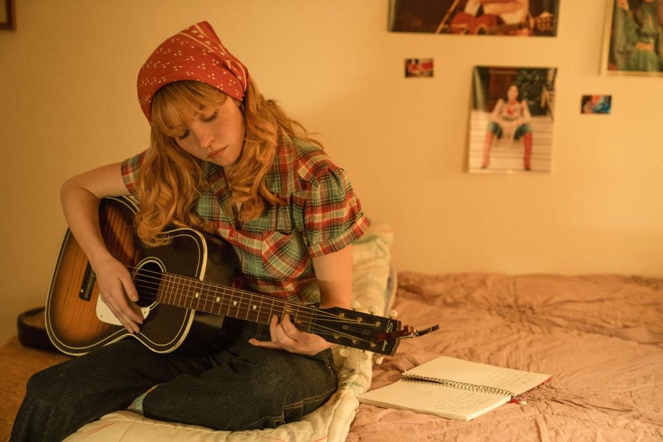 Woman playing acoustic guitar on bed.