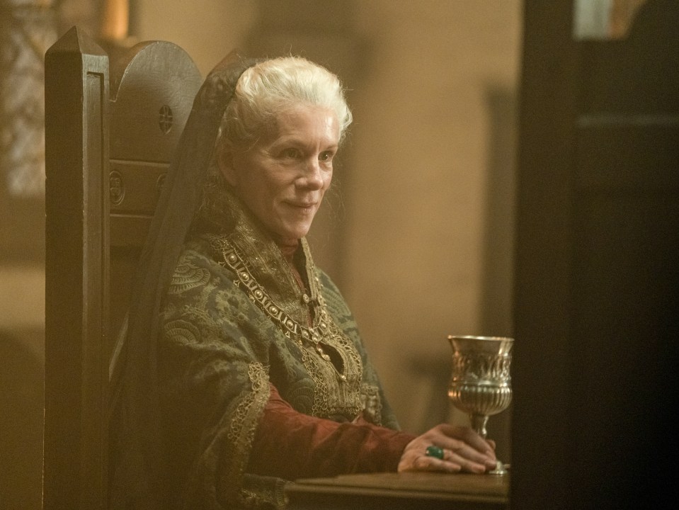 A woman in medieval-style clothing sits at a table, holding a goblet.