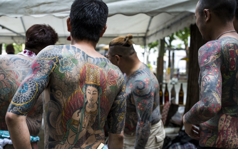 Yakuza members displaying tattoos at a festival.