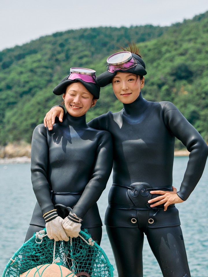 Two Haenyo women in Jeju, South Korea, wearing wetsuits and holding a net.