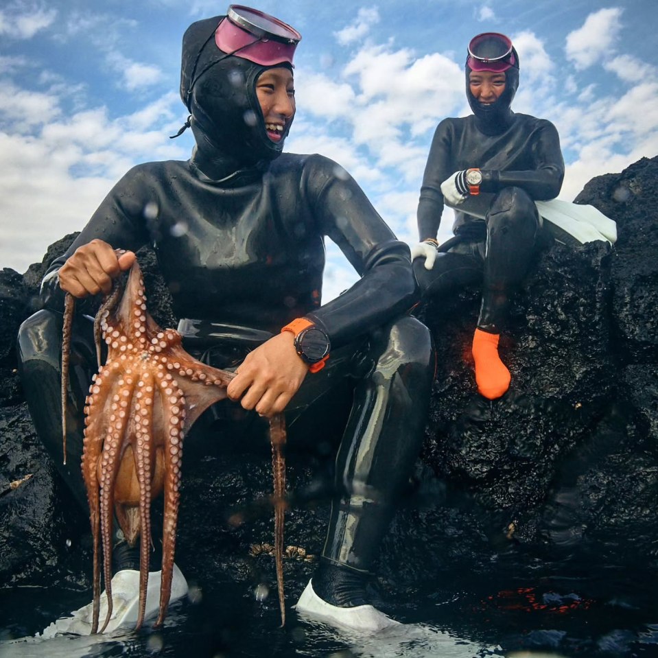 Two women in wetsuits holding an octopus after freediving.