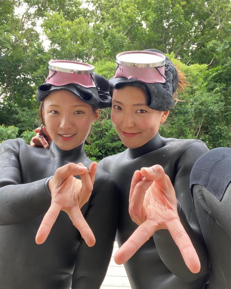 Two Haenyo women in Jeju, South Korea, wearing wetsuits and diving masks.