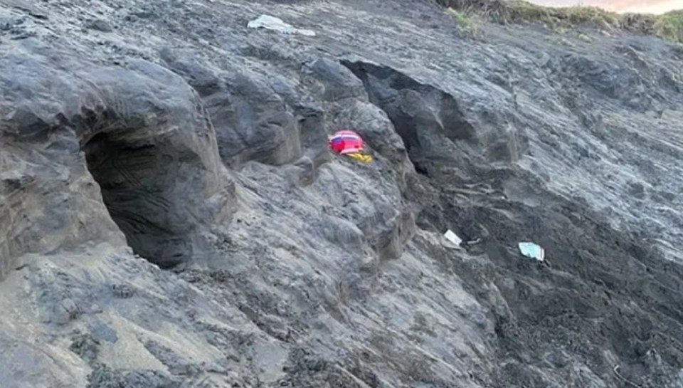 Sand dune collapse at beach, near children's belongings.