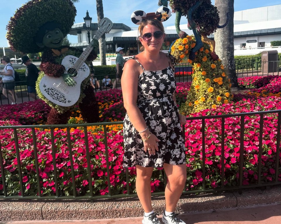 Woman in a floral dress at Disney World, posing in front of floral topiaries.