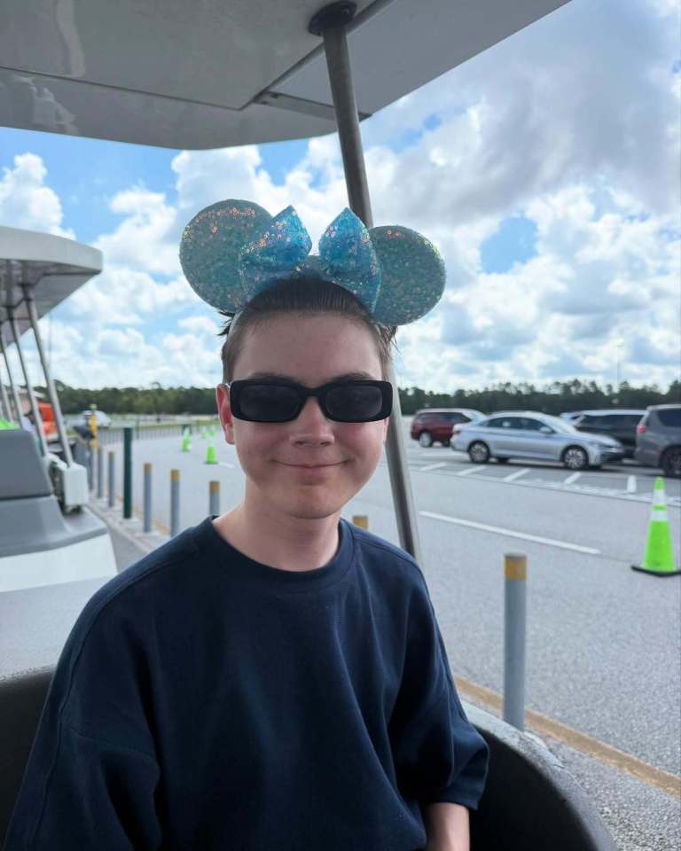 A young person wearing Minnie Mouse ears and sunglasses sits in a vehicle.