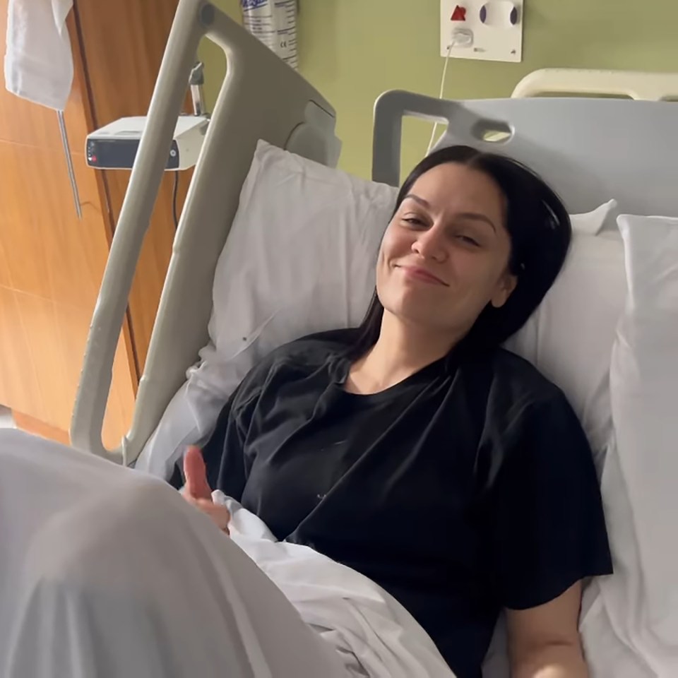 Jessie J in a hospital bed, giving a thumbs up.