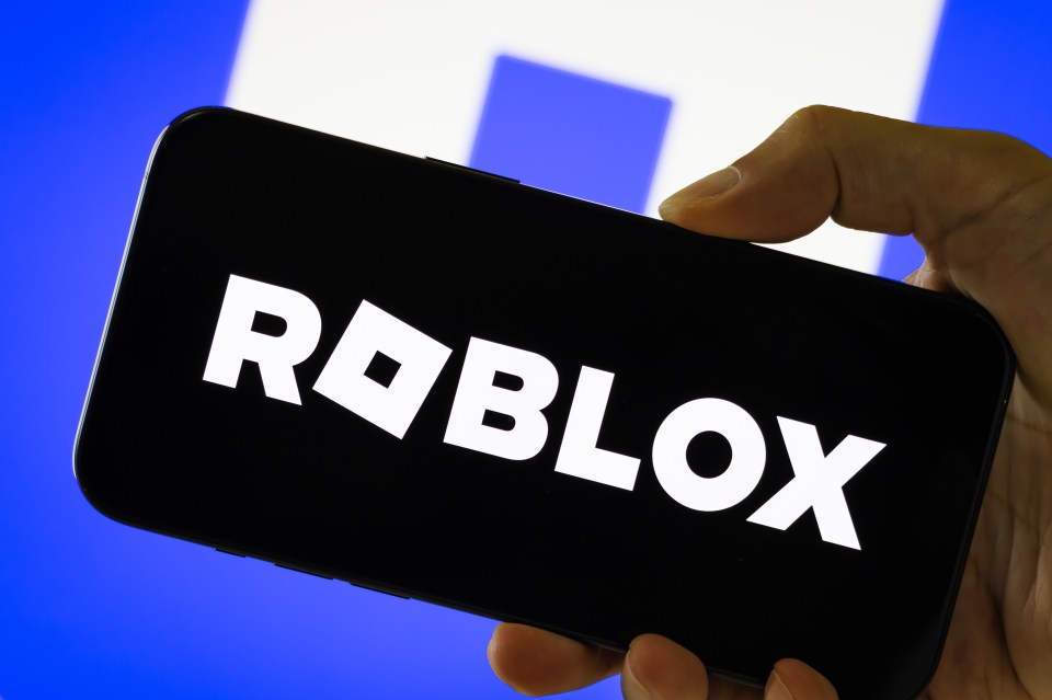 Photo illustration of a person holding a smartphone displaying the Roblox logo.