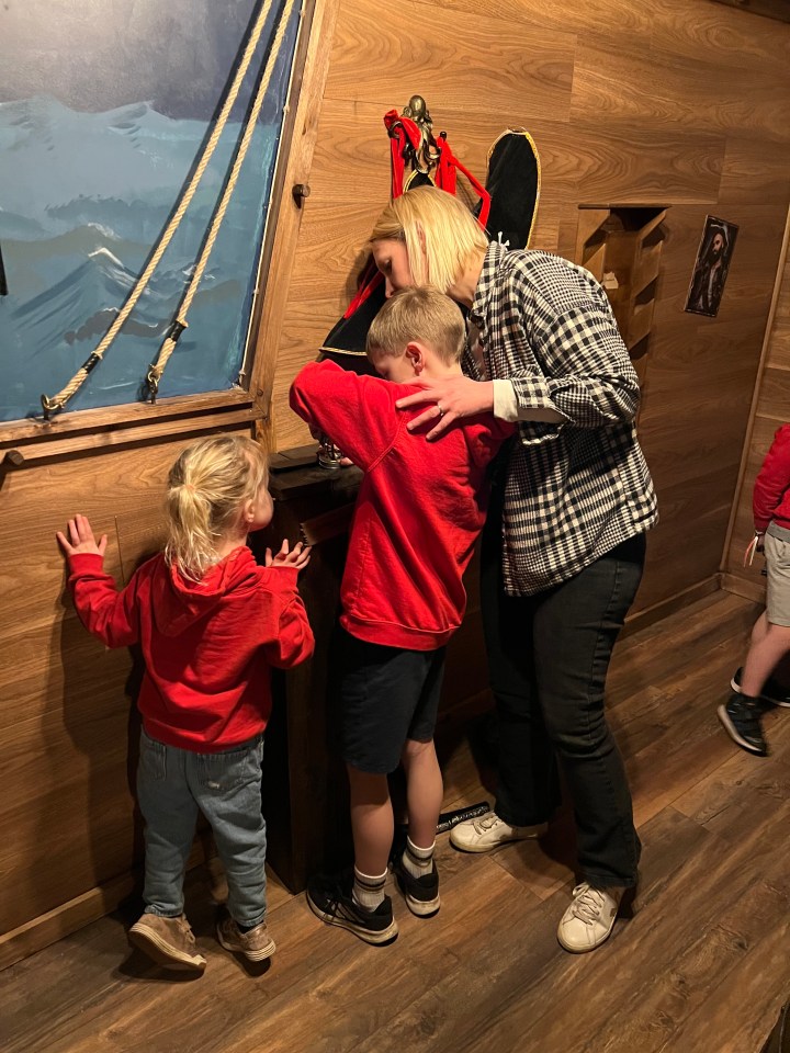 A woman and two children looking at something in a pirate-themed room.